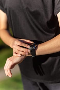 Teenage girl in black clothes checking her fitness watch after a workout. Tired runner girl controlling pulsations checking smartwatch.