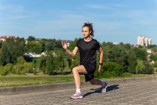 Young, fit and sporty girl in black clothes stretching after the workout in the urban city park. Fitness, sport, urban jogging and healthy lifestyle concept.