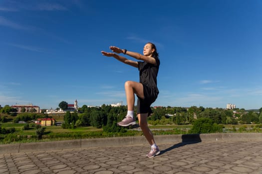 Young, fit and sporty girl in black clothes stretching after the workout in the urban city park. Fitness, sport, urban jogging and healthy lifestyle concept.