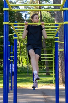 Portrait of beautiful teen age athletic girl training outdoors at open air gym at summer sunny day, gain hands muscles on horizontal bar. fitness, healthy lifestyle.