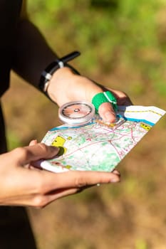 Woman holding a map and the compass during orienteering competitions. Athlete uses navigation equipment for orienteering,compass and topographic map.