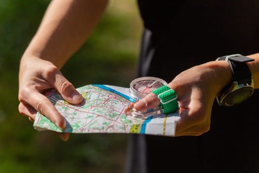 Woman holding a map and the compass during orienteering competitions. Athlete uses navigation equipment for orienteering,compass and topographic map.