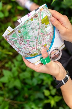 Woman holding a map and the compass during orienteering competitions. Athlete uses navigation equipment for orienteering,compass and topographic map.