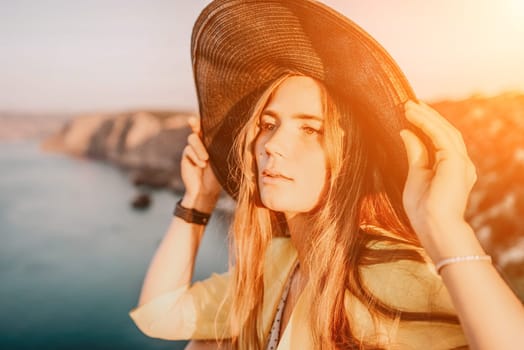 Portrait of happy young woman wearing summer black hat with large brim at beach on sunset. Closeup face of attractive girl with black straw hat. Happy young woman smiling and looking at camera at sea