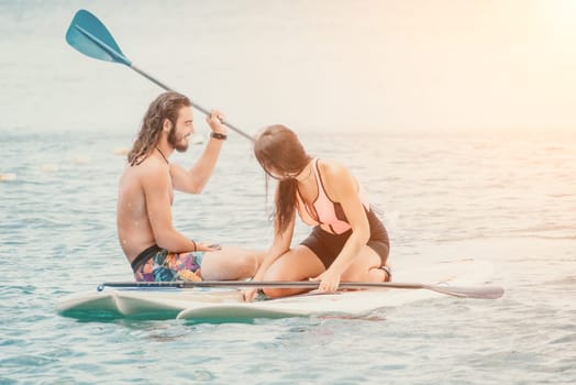 Sea woman and man on sup. Silhouette of happy young woman and man, surfing on SUP board, confident paddling through water surface. Idyllic sunset. Active lifestyle at sea or river