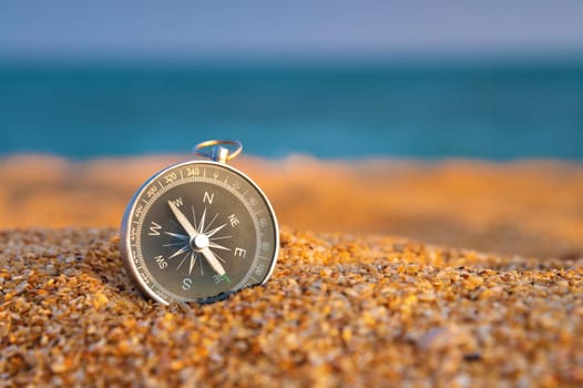 Close up, compass on sand, sea on background in daylight. Finding navigation while traveling along the sea coast.