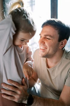 Smiling dad holds the waist of a little girl standing on the bed. High quality photo