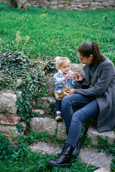 Little girl sits on stone steps in the garden with her mother and shows her hands. High quality photo