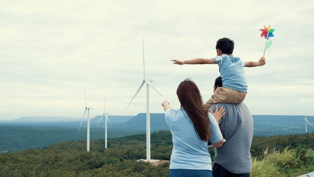 Concept of progressive happy family enjoying their time at the wind turbine farm. Electric generator from wind by wind turbine generator on the country side with hill and mountain on the horizon.