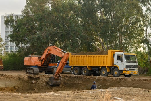 an excavator digs a hole under the foundation of a house and loads the earth into a dump truck