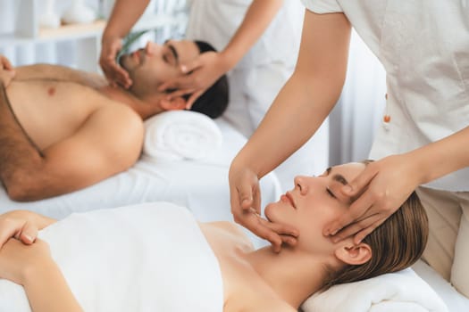 Caucasian couple enjoying relaxing anti-stress head massage and pampering facial beauty skin recreation leisure in dayspa modern light ambient at luxury resort or hotel spa salon. Quiescent