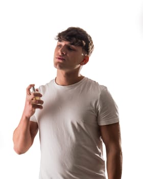 A man in a white shirt holding a perfume bottle, spraying it onto his neck. Handsome Man in a White Shirt Spraying Cologne