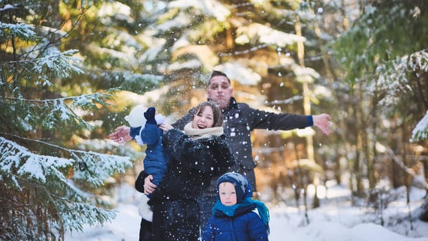 A happy family enjoying a winter sunny day in the woods. Father tosses snow