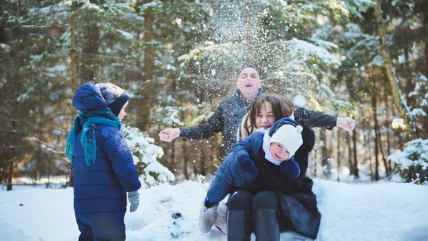 A happy family enjoying a winter sunny day in the woods. Father tosses snow