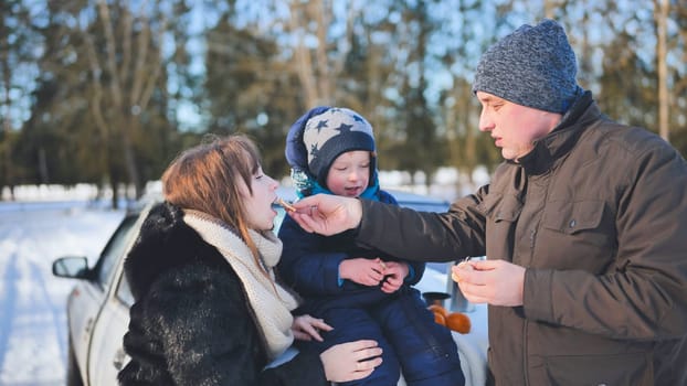 A young family is eating tangerines during a picnic on a winter day