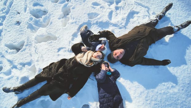 A young family lies in the snow on a sunny day