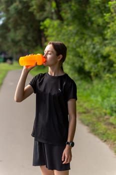 Fit tennage girl runner outdoors holding water bottle. Fitness woman taking a break after running workout.