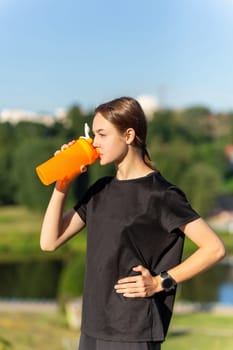 Fit tennage girl runner outdoors holding water bottle. Fitness woman taking a break after running workout.