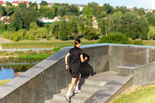 A young woman in black clothes running on stairs at city street early morning.