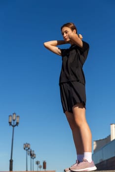 Young, fit and sporty girl in black clothes stretching after the workout in the urban city park. Fitness, sport, urban jogging and healthy lifestyle concept.