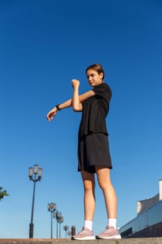 Young, fit and sporty girl in black clothes stretching after the workout in the urban city park. Fitness, sport, urban jogging and healthy lifestyle concept.