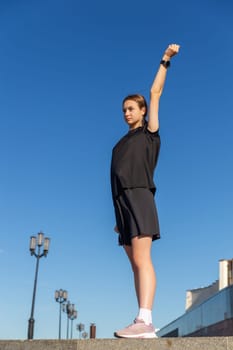 Young, fit and sporty girl in black clothes stretching after the workout in the urban city park. Fitness, sport, urban jogging and healthy lifestyle concept.