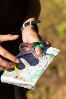 Woman holding a map and the compass during orienteering competitions. Athlete uses navigation equipment for orienteering,compass and topographic map.