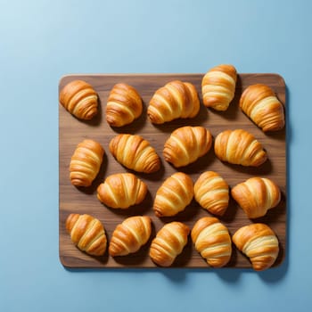 Freshly baked croissants on a wooden board next to a cup of hot coffee on a blue background