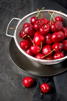 Cherry summer background. A large number of cherries with leaves on the table in a saucepan on a black background.