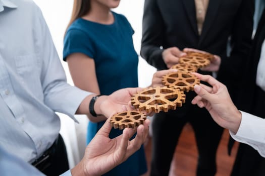 Office worker holding cog wheel as unity and teamwork in corporate workplace concept. Diverse colleague business people showing symbol of visionary system and mechanism for business success. Concord