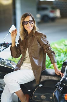 Middle aged woman with sunglasses sitting on a vintage motorcycle. Caucasian female in urban background.