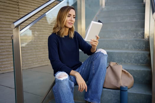 Middle-aged woman reading with her e-book on a coffee break near her office. Caucasian female wearing casual clothes.