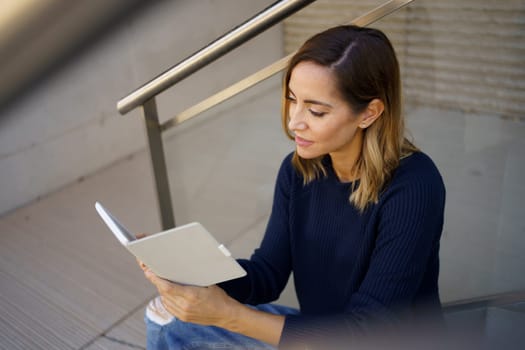 Middle-aged woman reading with her e-book on a coffee break near her office. Caucasian female wearing casual clothes.