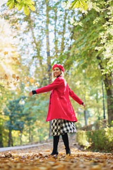 Full body side view of positive female in red clothes spinning around while standing on alley with dried leaves in autumn park