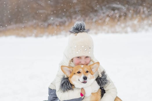 A Young happy woman having fun in snowy winter park with Corgi baby dog