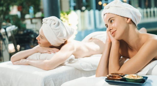 A couple of beautiful young woman relaxes on a spa bed surrounded by nature at outdoor. ready for a body massage. Attractive females in white towels lie on bed peacefully. Close up. Tranquility