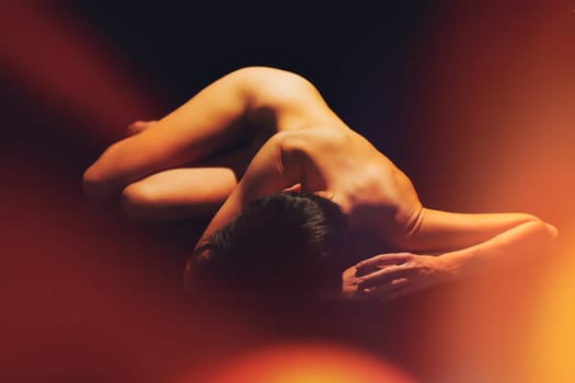 Full body of anonymous fit naked woman with short dark hair lying on floor against black background in studio