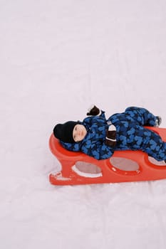 Little boy resting lying on a sled in the snow. High quality photo