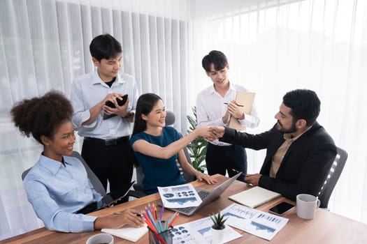 Diverse coworkers celebrate success with handshake and teamwork in corporate workplace. Multicultural team of happy professionals united in solidarity by handshaking in office. Concord