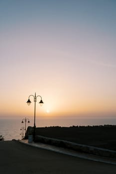 Lanterns along the road descending to the sea at sunset. High quality photo