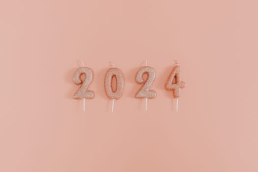 Shiny candles with the number 2024 lie in a row in the center on a pink background, flat lay close-up.