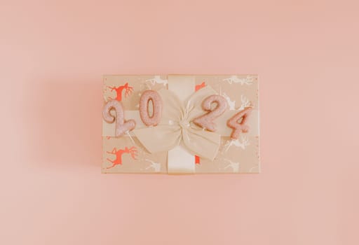 Shiny candles with the number 2024 on a gift box tied with a bow lie in the center on a pink background, flat lay close-up.