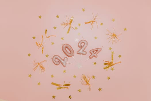Shiny candles number 2024 with gold tinsel and confetti lie in a round frame in the center on a pink background, flat lay close-up.