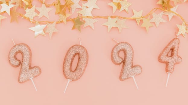 Shiny candles number 2024 with a festive gold garland in the shape of stars lie on a pink background, flat lay close-up.