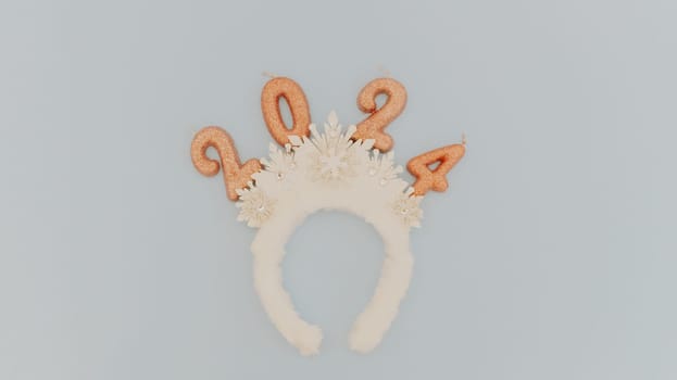 Cute baby headband tiara with white snowflakes and light brown sparkly candles number 2024 lie in the center on a pastel blue background with copy space on the sides, flat lay close-up.