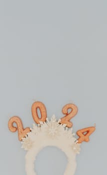 Cute baby headband tiara with white snowflakes and light brown sparkly candles number 2024 lie in the bottom on a pastel blue background with copy space on top, flat lay close-up.