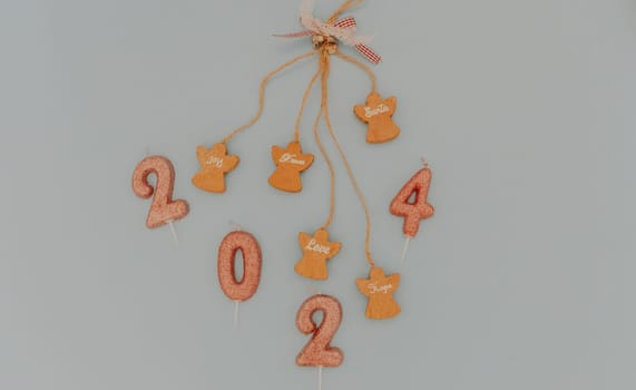 One holiday decoration with wooden angels, motivational words hanging on a blown string and light brown glitter candles number 2024 lies in the center on a pastel blue background, flat lay close-up.