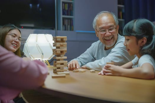 Happy grandparents Asian family enjoy playing toy block with little daughter together in home living room at night time, Smiling parent having fun play build constructor tower of wooden blocks