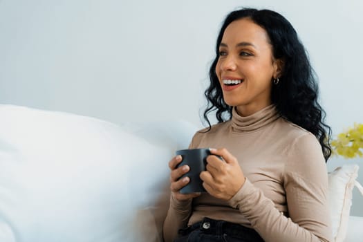 Happy woman drinking coffee on a sofa at home for crucial rest and relaxation. Portrait of young African American woman holding a cup.