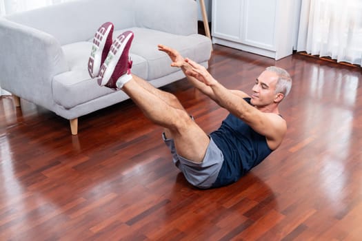 Athletic and sporty senior man doing exercise on the floor targeting ABS at home exercise as concept of healthy active fit body lifestyle after retirement. Clout